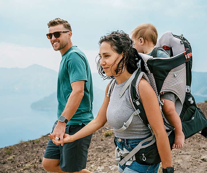 Couple hiking while holding hands with a baby in a carrier backpack