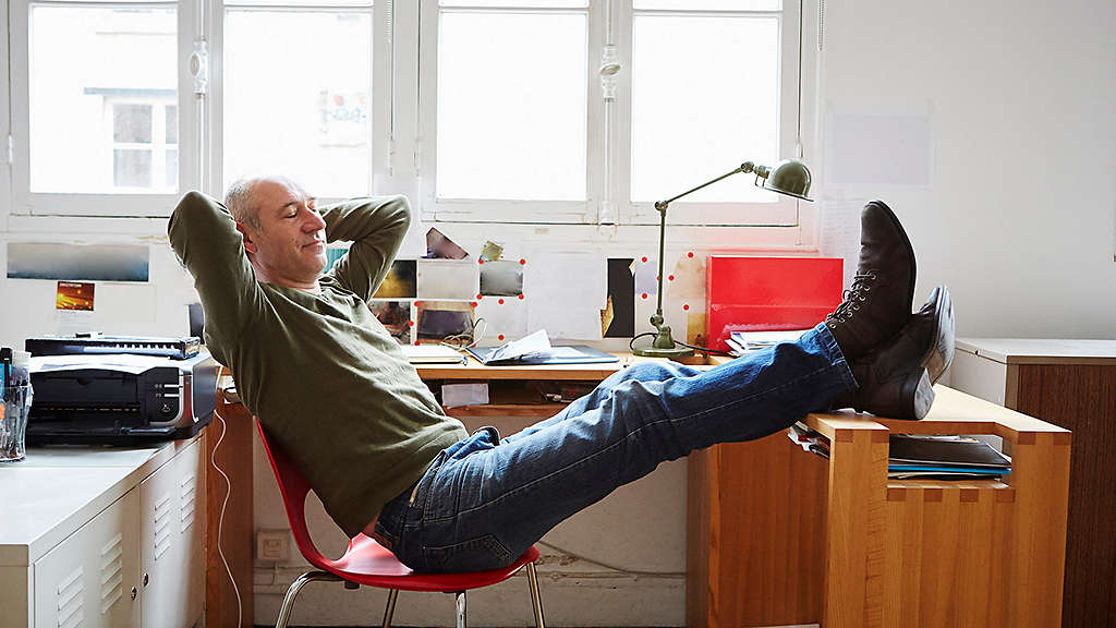Person contemplating while leaning back in chair with hands behind their head  and feet propped up on their desk