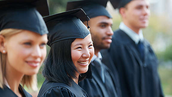 Young college graduates holding their diplomas while standing in a row and smiling