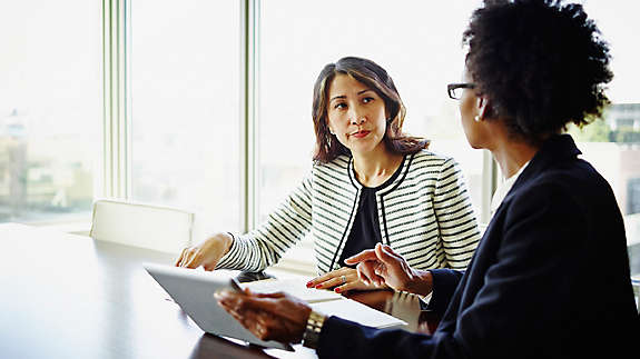 Two businesswomen discussing project details on digital tablet at conference table
