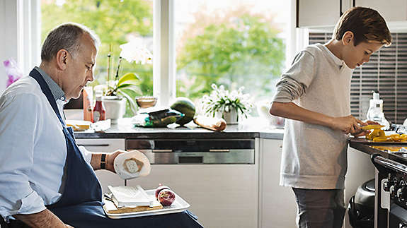 Middle-aged gentleman and son cooking together in kitchen