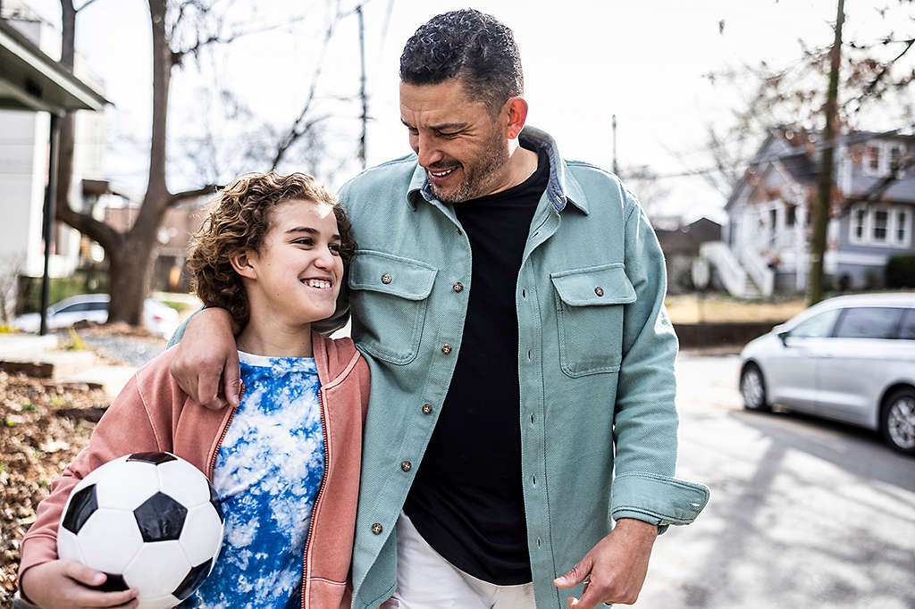 Father and son holding soccer ball walking down suburban street