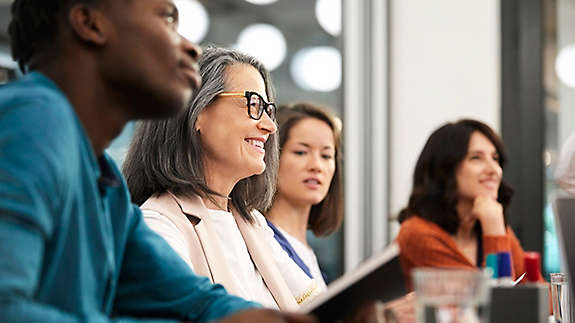 Smiling mature businesswoman sitting with colleagues in a meeting.
