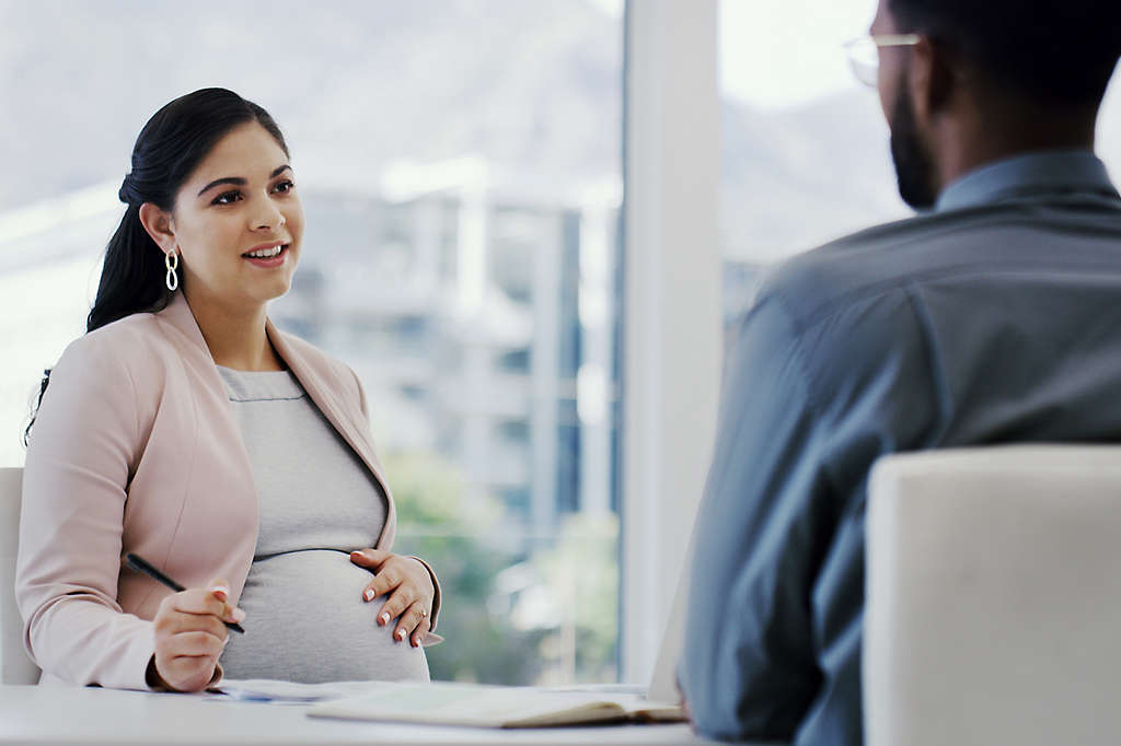 Woman touching her pregnant belly while sitting in an office meeting