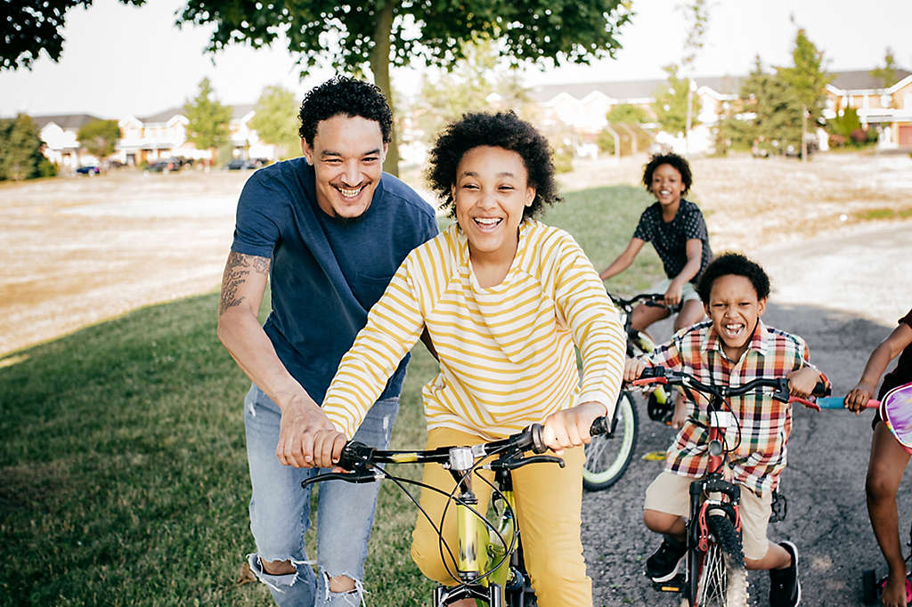 Parent helps teenage child balance on bike as they ride with other children