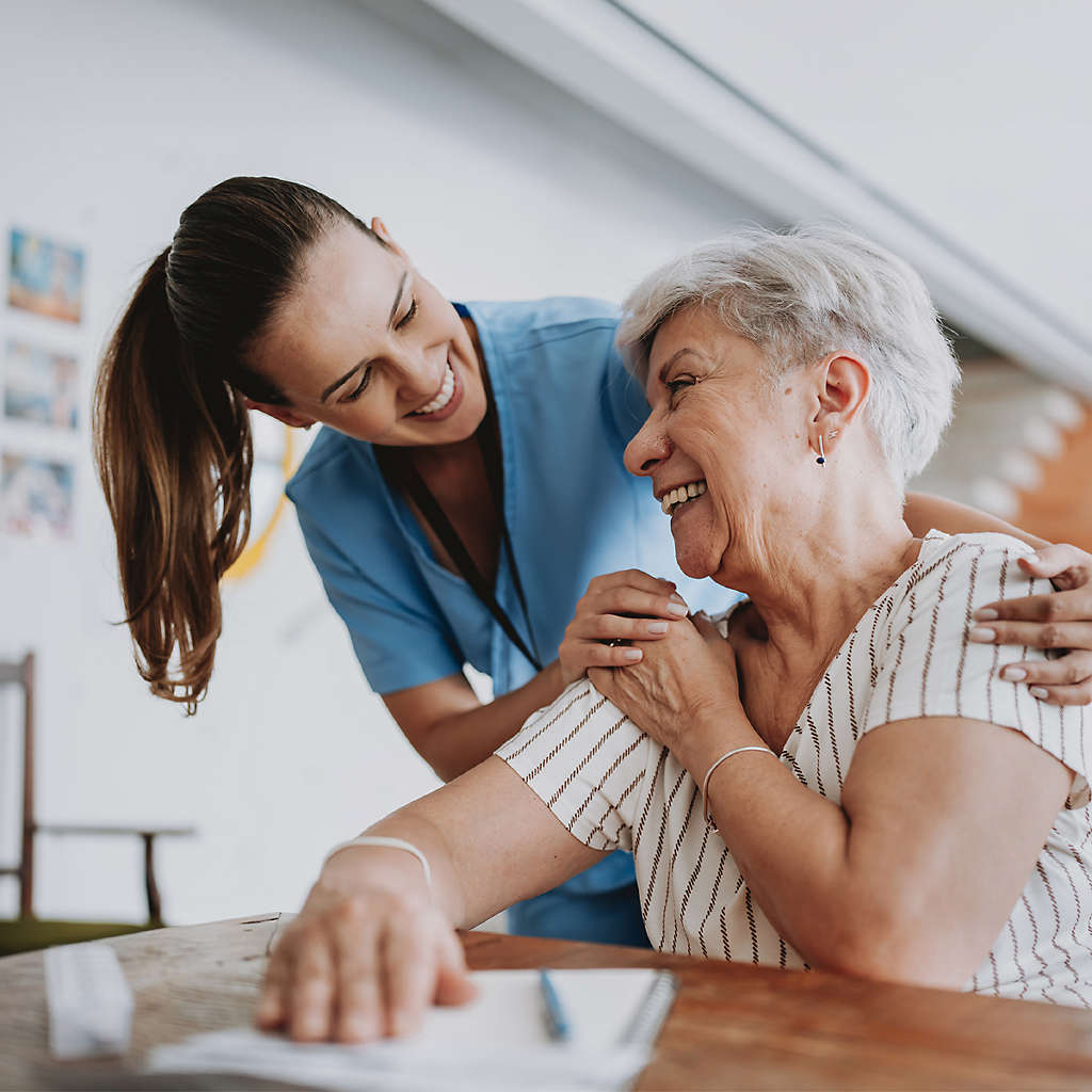 A healthcare worker smiling while embracing an older person