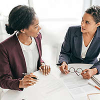 Two feminine-presenting professionals sitting at a table discussing business