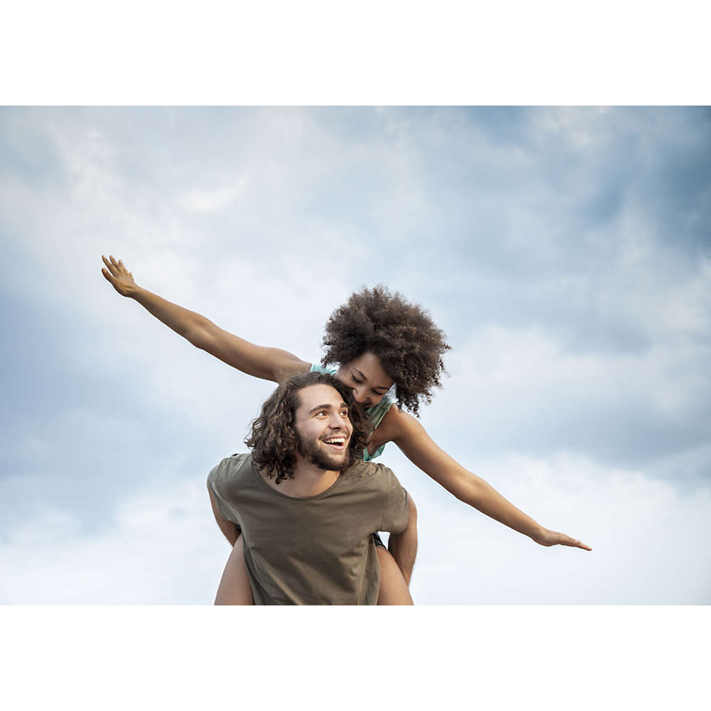 Couple outside with partner on piggyback flying against a sky background