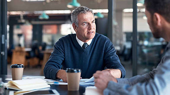 A business owner discusses succession planning with his partner at a boardroom table.�