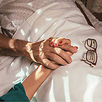 A daughter holds her father�s hand as he lies in a hospital bed.�