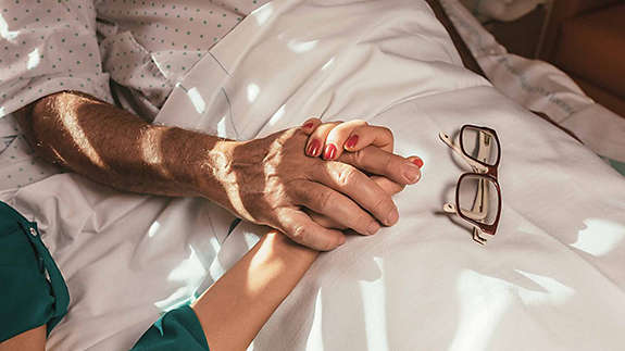 A daughter holds her father�s hand as he lies in a hospital bed.�