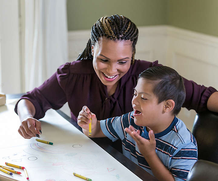 Caregiver supporting special needs child doing coloring activity