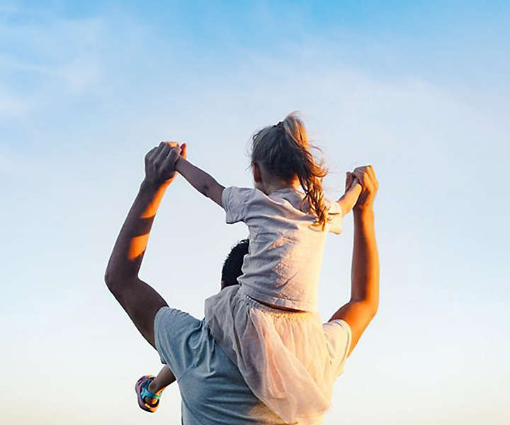 daughter sitting on father shoulders looking at sky