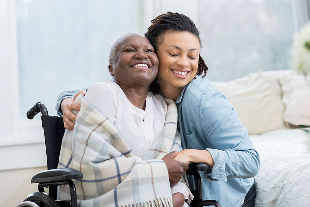 Granddaughter hugging grandmother in wheelchair and blanket in her home