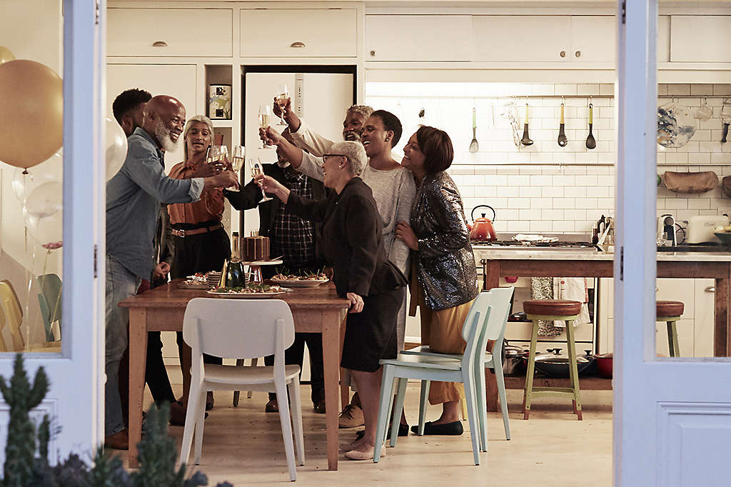 Family in large kitchen enjoying a birthday celebration raising flutes of champagne and toasting