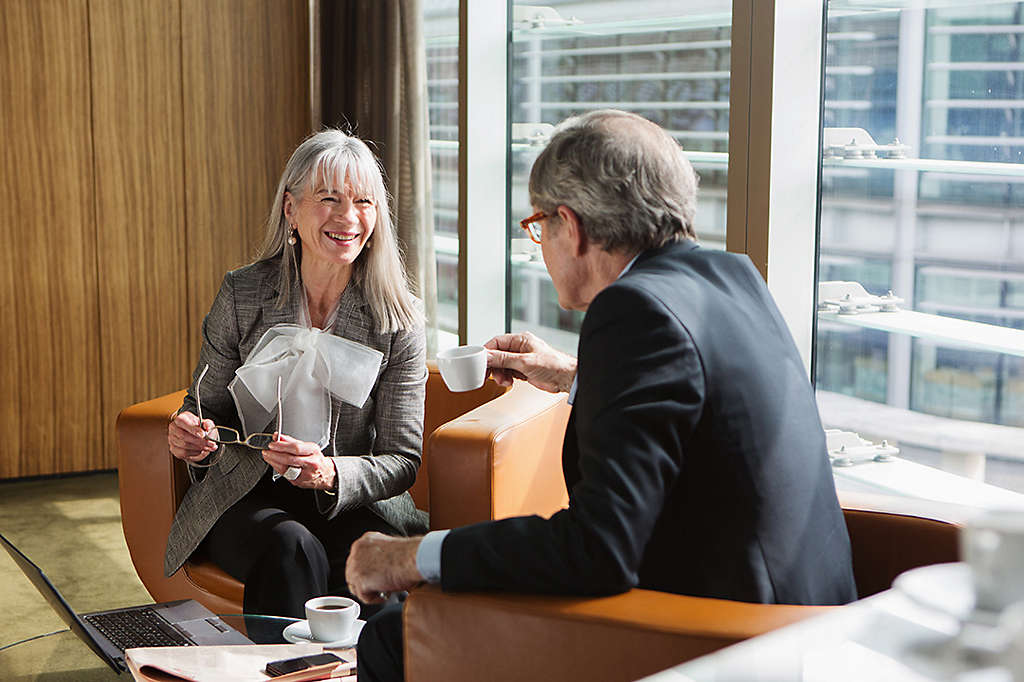 Two-older-professionals-chatting-over-coffee-in-a-modern-office-lounge