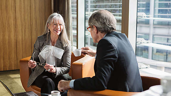 Two-older-professionals-chatting-over-coffee-in-a-modern-office-lounge
