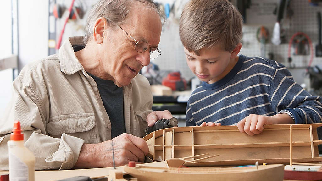 Grandfather enjoying building model boat in his workshop with his grandson