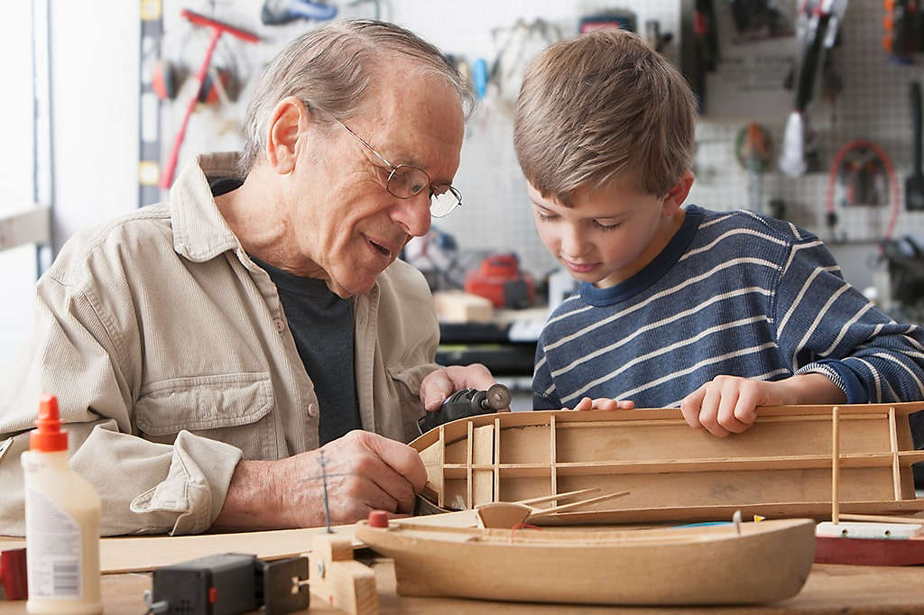 Grandfather enjoying building model boat in his workshop with his grandson