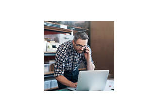 man working on laptop while conversing on a mobile phone