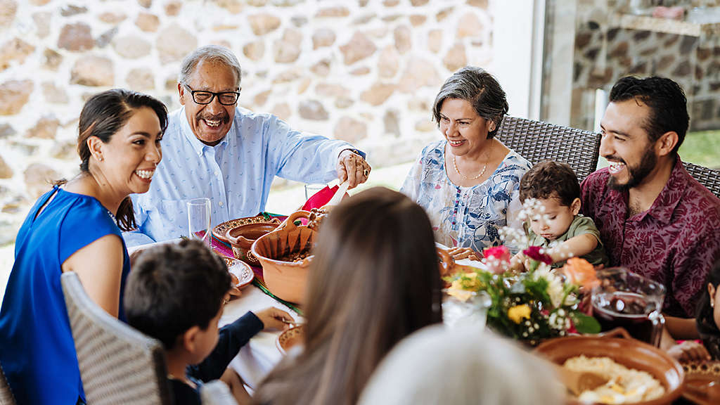 Latin senior man serving the food to his family at dinner table