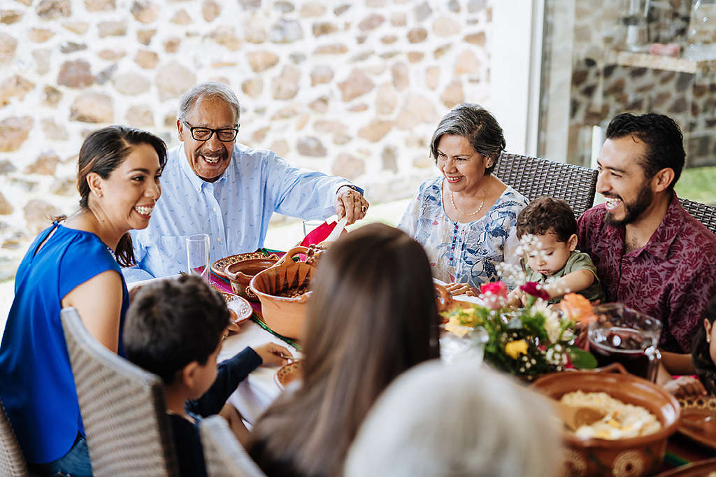 Latin senior man serving the food to his family at dinner table