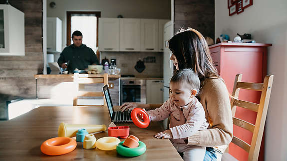 Mother holding a child while working on computer.