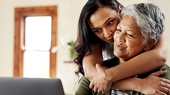 A mature woman being hugged by an older child while working on a computer.