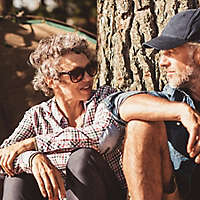 A mature couple sitting under a tree outside a camping tent