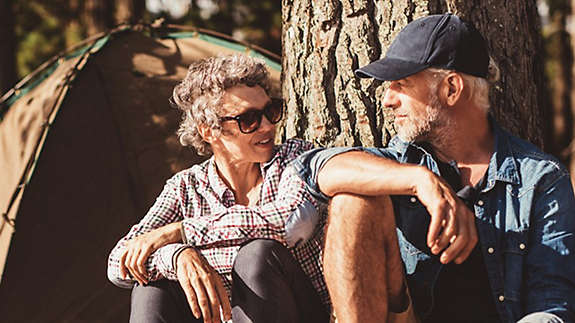 A mature couple sitting under a tree outside a camping tent