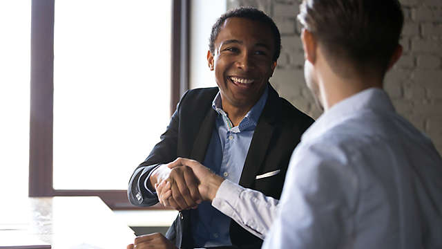 Two business professionals shaking hands at a desk