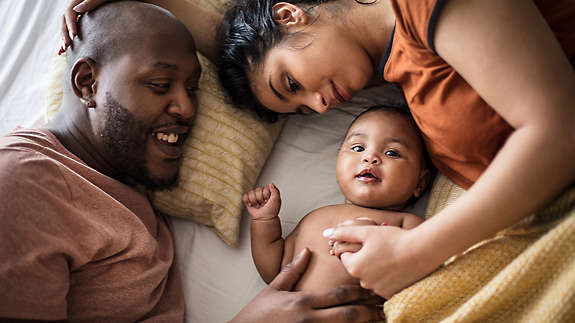 Mother and father laying on bed with their baby