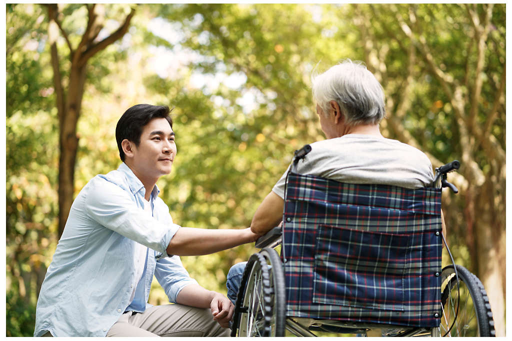 A man holding the hand of his father in a wheelchair