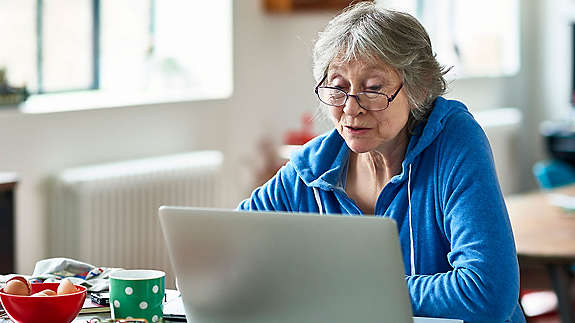 Caucasian woman in her 50s concentrating, peering at screen, working on home finances, planning for retirement