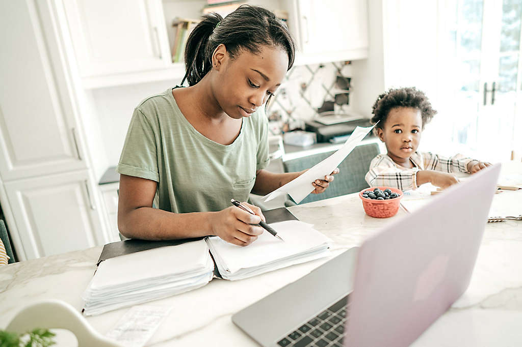 Mother doing paperwork; child in a highchair in the kitchen