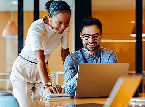 two happy employees looking at a laptop in a office setting